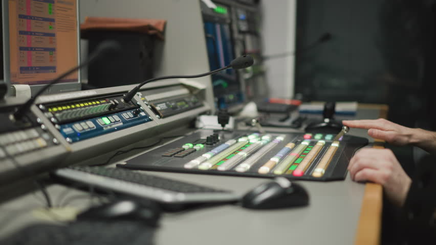 Close-up of hand operating video production switcher in broadcast studio. Professional television equipment with illuminated buttons and monitor in control room environment
