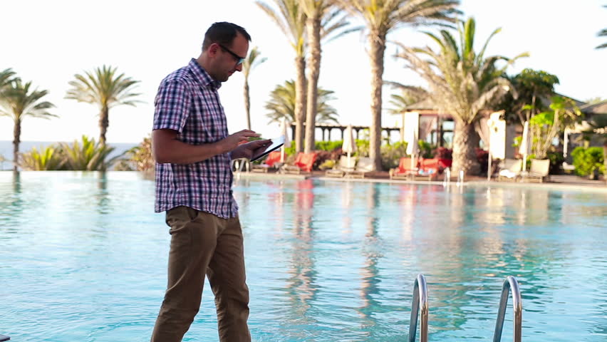 Happy young man with tablet computer walking by the pool
