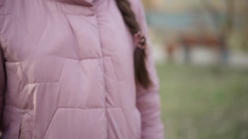 Close-up of person wearing light purple quilted winter jacket with braid partially visible, standing outdoors in blurred park background, representing cold weather clothing,and seasonal fashion