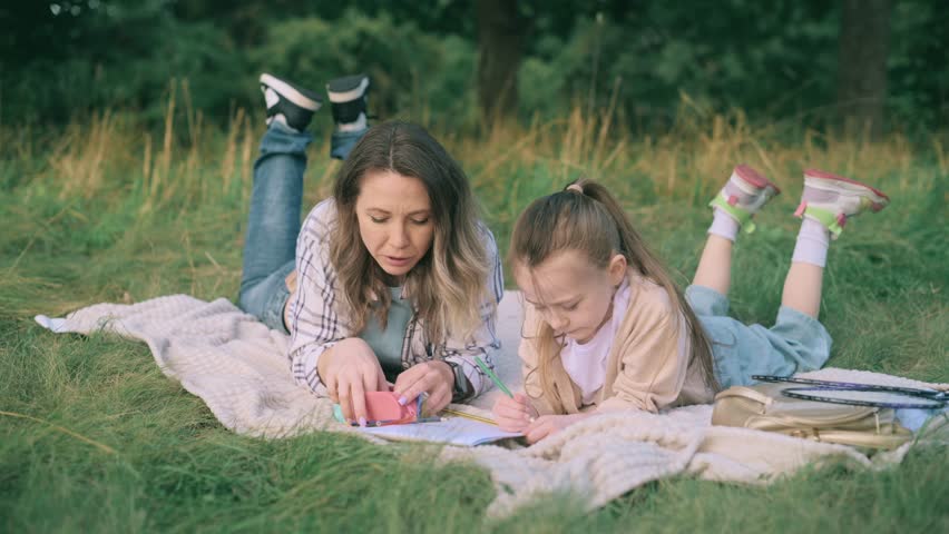 A woman spends time with her daughter. A mother and her four-year-old daughter draw with pencils in nature.