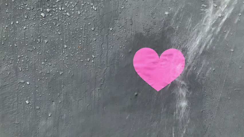 A paper heart is sprayed with water until its color and shape fade, in 4K footage, creating a poignant visual for a broken heart theme background