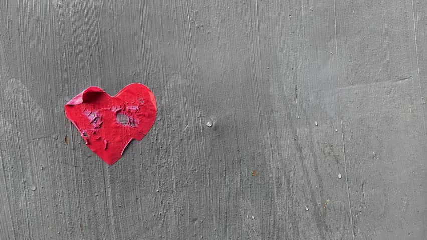 A hand wipes a paper heart on a wall until it fades away, creating a poignant visual for a broken heart theme, 4K footage broken heart background