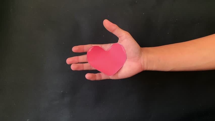 A hand forcefully crumples a paper heart, ruining its color and shape, with ample copy space for a broken heart theme, 4K footage