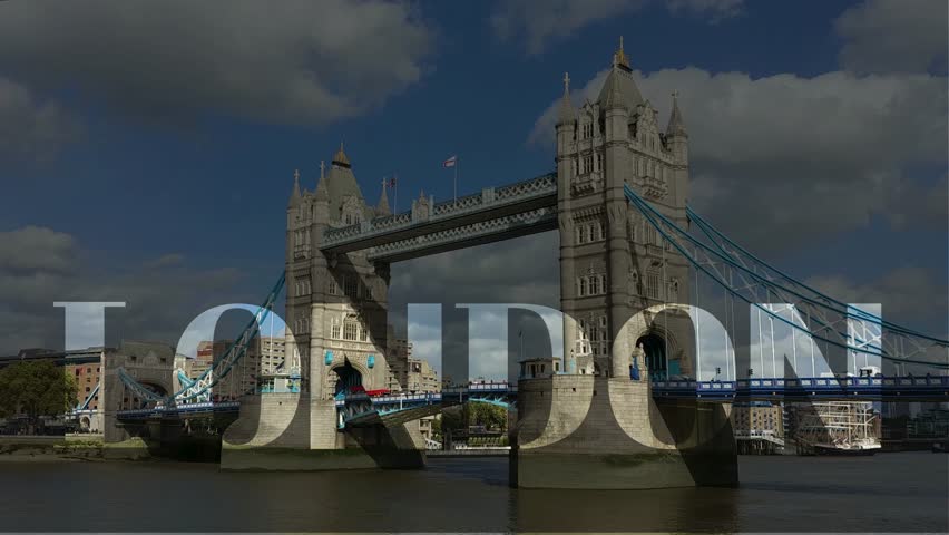 A scenic view of the Tower Bridge in London from across the River Thames, featuring its iconic twin towers and a double-decker bus crossing the bridge on a partly cloudy day.