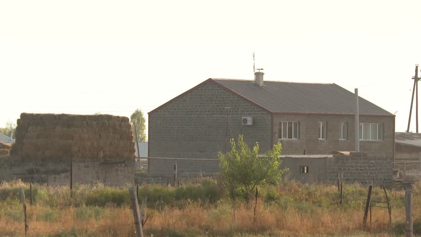 A peaceful rural village scene. Smoke rises from chimneys on a hazy morning with hay bales. A wide shot reveals the town is located on a rocky cliff.