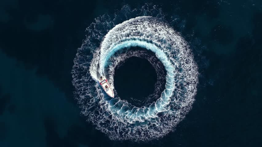 Aerial overhead view of a RIB speedboat turning circles on the water surface and driving away leaving a trail of surf and waves