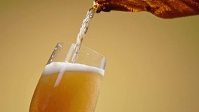 Cold craft light beer pouring in glass from bottle, slow motion close up. Stream wheat malt beverage flowing in clear goblet making dense bubbling foam. Froth heady drink foaming on yellow background - Powered by Shutterstock - Get 15% off with code: PIKWIZARD15