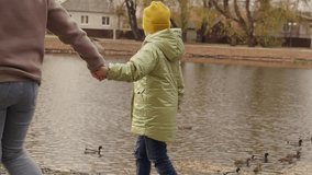Child holds his mother hand, they walk together to lake in autumn. People relax in nature. Happy family, daughter mother hold hands, walk in city autumn park near pond, child points to swimming ducks - Powered by Shutterstock - Get 15% off with code: PIKWIZARD15