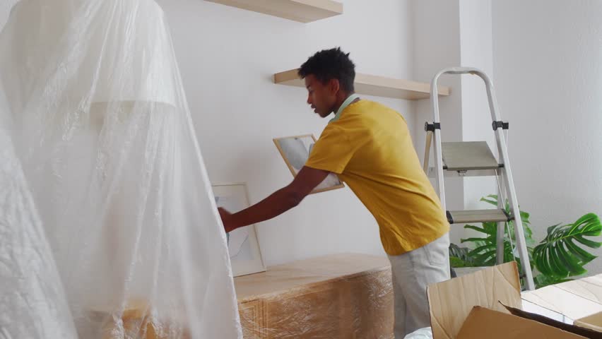 Young man decorating new apartment, hanging pictures on wall
