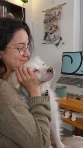Millennial freelance graphic designer working from home, sharing tender moment of companionship while embracing white dog during relaxing break