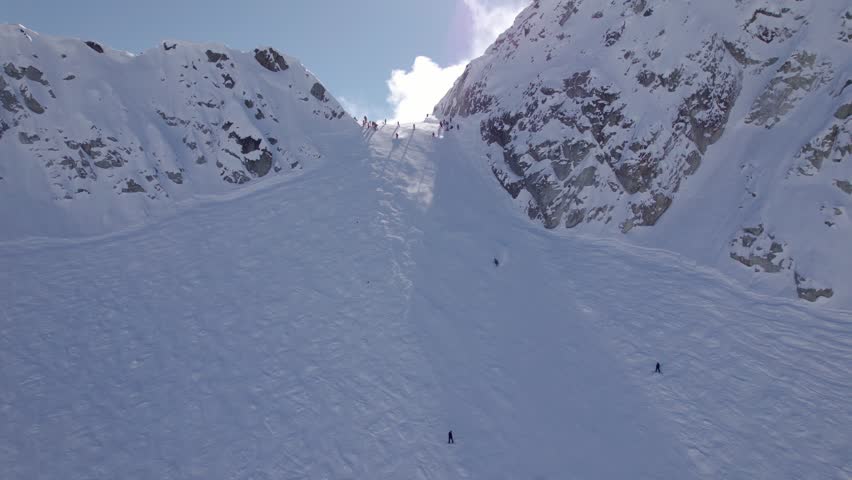 Aerial view of Whistler Mountain peak, downhill skiers, sunny snow covered peak, ski resort. 4K 24FPS