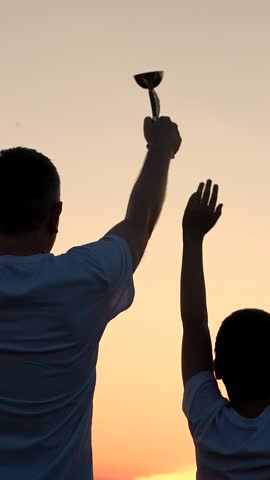 Joint victory of dad of little son champion. Father, child celebrates victory, winner in sport, life success concept. Silhouette happy champion, sporty little boy dad holding golden cup in hands, sky