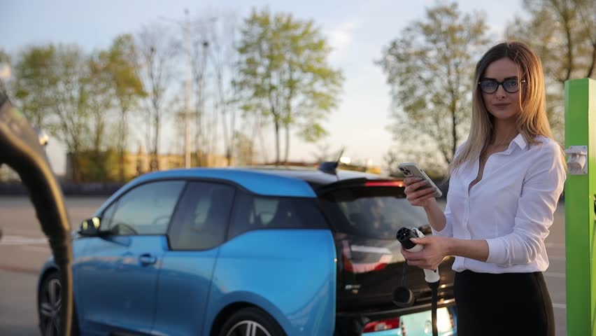 Portrait of a beautiful young business woman holding an electric car charger while standing outdoors