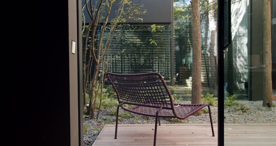 A contemporary wicker chair placed on a wooden deck, overlooking a tranquil garden scene, captures a serene outdoor setting. Modern Wicker Chair on Serene Wooden Deck With Garden View