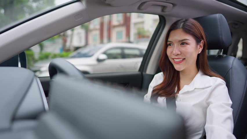 Beautiful Asian woman fastening her seatbelt while driving a car. Attractve young woman employee sit inside the vehicle, feel happy and enjoy showing safe and protected driving while driving to work.