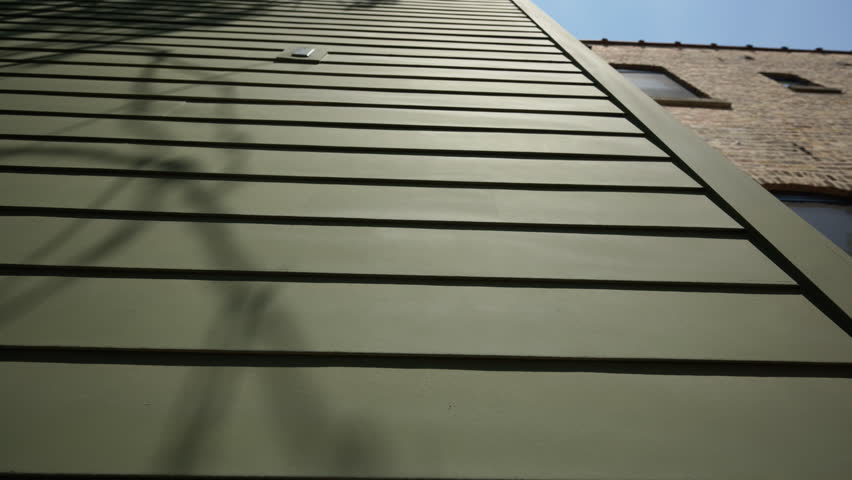 Wide view of green siding of the house wall with modern panels, providing a sleek and classic exterior look on sunny day. move camera view