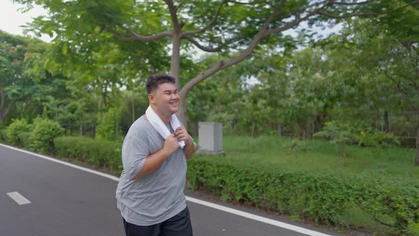 Asian plus-size man exercises outdoors in the garden to lose weight. Attractive young overweight guy spend leisure time on weekend doing running workout to improve health and overall fitness in park.