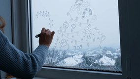 Creative enthusiastic unrecognizable woman in sweater paint window with white marker. Christmas tree decoration on big clear window. Snowy winter outside - Powered by Shutterstock - Get 15% off with code: PIKWIZARD15