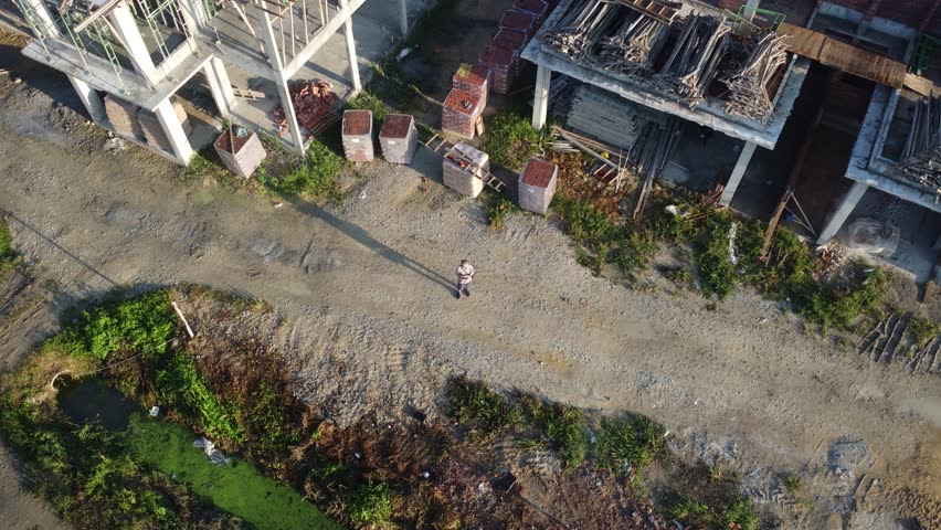 Aerial footage of a man model flying drone around the residence houses with a small vacant plot of land under construction. 