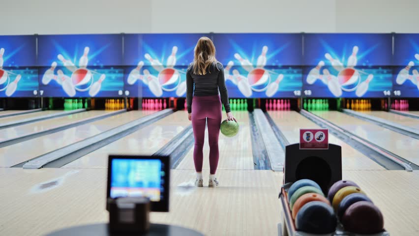 Focused woman prepares to throw bowling ball in lane during leisure game