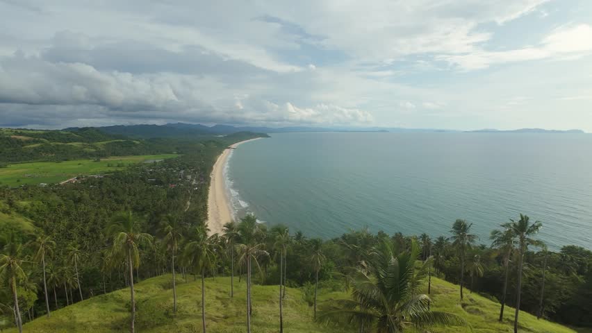 Dynamic FPV drone shot flying forward over palm-covered hills at Bato ni Ningning toward Long Beach, the longest beach in Palawan, Philippines.