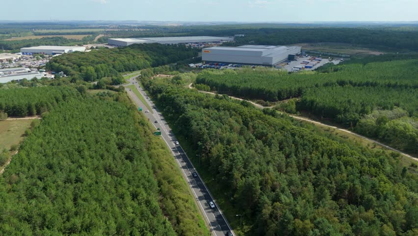 Aerial drone view of road cutting through Sherwood forest, Nottingham and large industrial distribution centre sunny day England UK