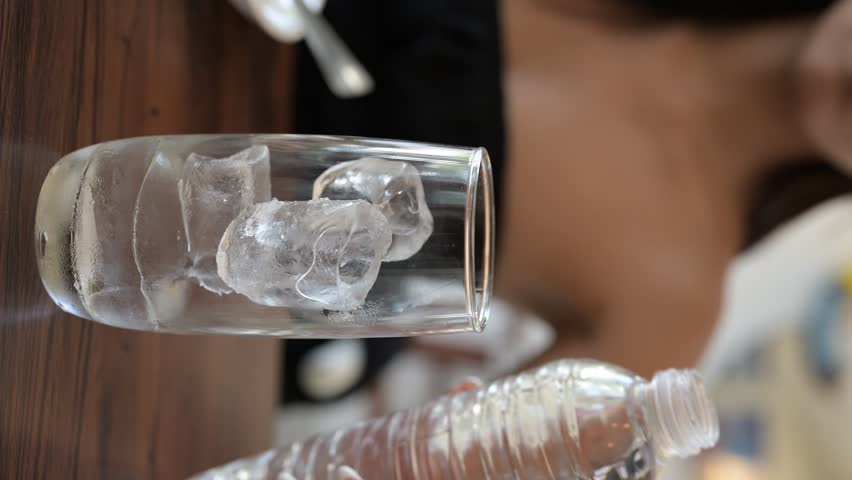 Vertical portrait video of young woman pouring water to glass with ice inside restaurant during day