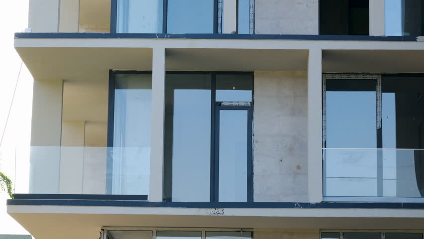 Slider shot of Interior view of a spacious, unfinished room featuring large glass windows that let in natural light, providing a view of greenery, giving an impression of future potential and openness