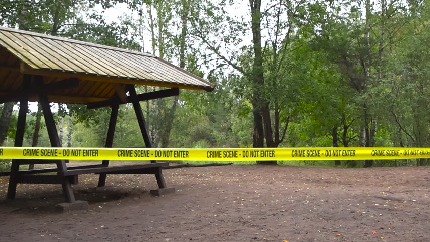 Yellow police line or Crime scene forensics investigation tape ribbon pulled in front of a outdoors camping area with a lake or a river in the forest background. Tape is in focus, background bokeh.