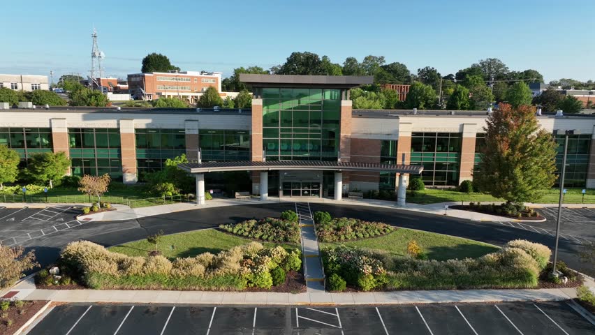 Centra Lynchburg general hospital entrance with green transparent windows in Virginia. Aerial view. Red brick buildings during sunset time in the evening. Empty driveway in front of door.