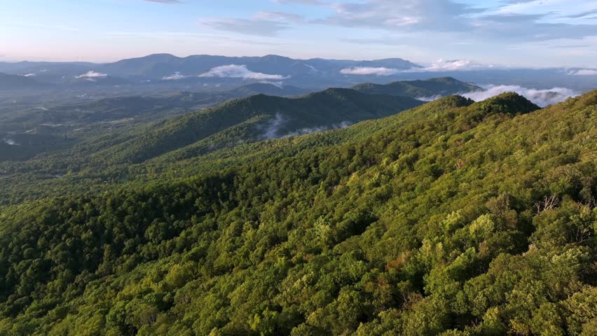 Beautiful mountain landscape with green hills and blue sky. Aerial wide shot. Flying clouds and fog between Mountain at sunset. Panorama view.