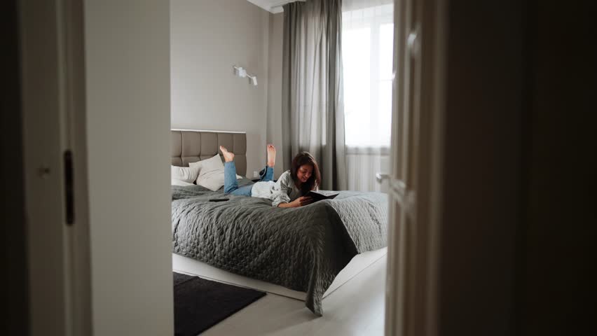 Woman enjoys reading a book on her bed in a stylish bedroom during the afternoon