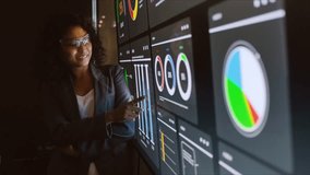 Smiling professional stands by large digital dashboards with charts, graphs, and metrics. Modern office scene features analytics, data visualization, reporting, statistics, and technology tools. - Powered by Shutterstock - Get 15% off with code: PIKWIZARD15