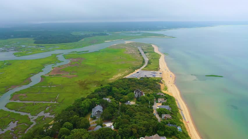 Aerial drone footage of Cape Cod public beach where cars in the lot highlight shoreline access, with the Atlantic horizon beyond, balancing community activity and scenic natural coastal beauty.
