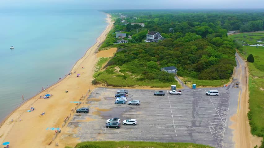 Wide aerial view of Cape Cod public beach with cars and shoreline access, blending the natural Atlantic coastal landscape with parking facilities that support visitors enjoying the seaside scenery.
