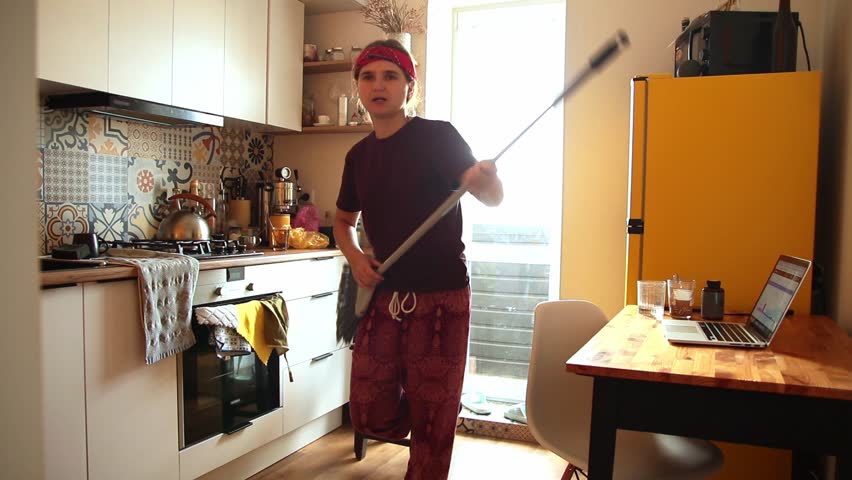 Creative Procrastination. A Hipster Woman Singing and Playing with a Broom. A Hipster Woman Dancing and Singing in a Modern Kitchen.