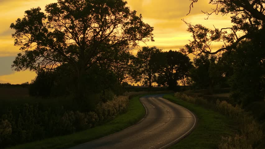 Car driving on countryside road during sunset. Road trip, car traveling, countryside driving, sunset vacation. Vehicle moving on rural roadway at sundown