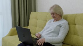 Elderly woman in light gray sweater sitting comfortably on yellow sofa with black laptop, symbolizing online learning, mentoring and remote work. - Powered by Shutterstock - Get 15% off with code: PIKWIZARD15