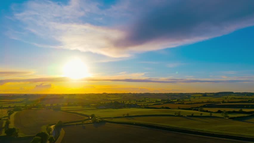 Sunset time lapse with glowing sun over agricultural countryside landscape captured from drone. Evening timelapse with dramatic orange sky and rolling farmland aerial view. Golden hour with bright