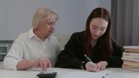 Senior woman in white vest teaching teen girl in black hoodie at desk with notebook and calculator, symbolizing mentoring, study, and education - Powered by Shutterstock - Get 15% off with code: PIKWIZARD15