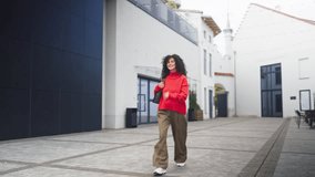 Caucasian curly haired cheerful woman in red sweater and wide pants walking with bag on shoulder in modern courtyard. Confident happy female smiling while strolling outdoors in casual outfit. - Powered by Shutterstock - Get 15% off with code: PIKWIZARD15