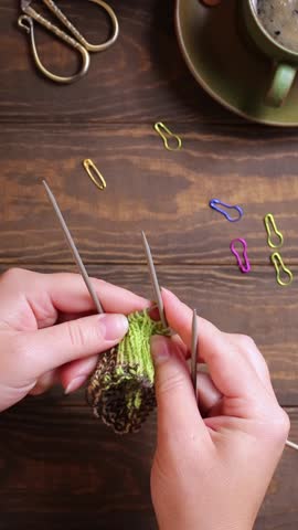 Flat lay with female hands knitting green socks in progress. Cozy homely atmosphere with wooden table and cup of coffee. FullHD footage vertical video