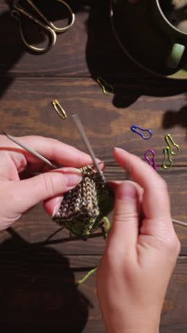 Flat lay with female hands knitting green socks in progress. Cozy homely atmosphere with wooden table and cup of coffee. FullHD footage vertical video. Hard light