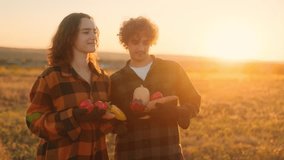 Two young farmers, man and woman, stand in a rural field at golden sunset holding fresh vegetables in their hands, smiling and enjoying country life together. - Powered by Shutterstock - Get 15% off with code: PIKWIZARD15