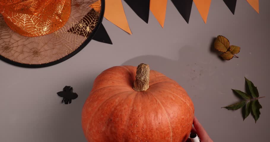 A person draws the face of a pumpkin with a marker. Decorations, including a witch