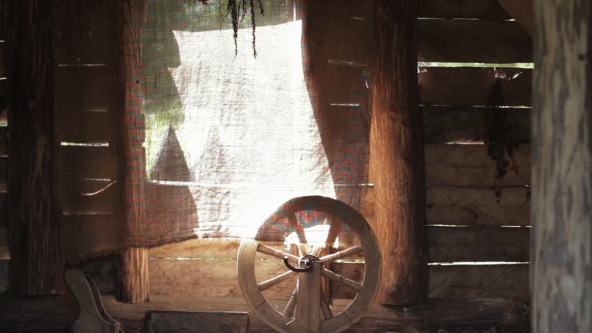 Interior of an old village house with a spinning wheel window in the background. Wooden hut with dried herbs on the walls, background