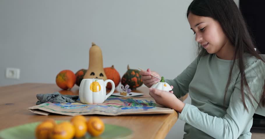 Happy young girl painting pumpkin glass cup for Halloween party - Holiday, childhood and autumn lifestyle concept