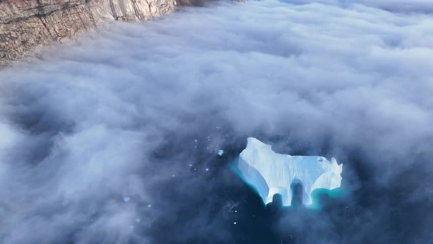 Town Uummannaq during summer in northern West Greenland beyond the Arctic Circle. Greenland, Danish territory. Large mountains and glaciers in the background. Misty morning. Fjord in Greenland. Aerial