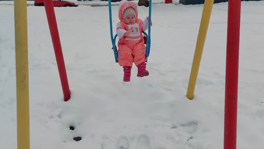 little cauacasian girl riding on a swing in winter during snowfall
