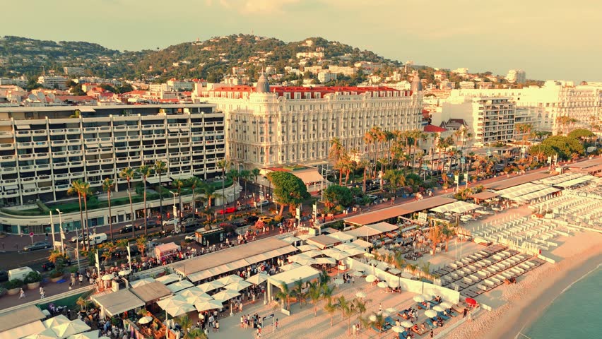Aerial pan shot featuring Carlton Cannes hotel located at sea shore with cityscape of Cannes in france during sunset.